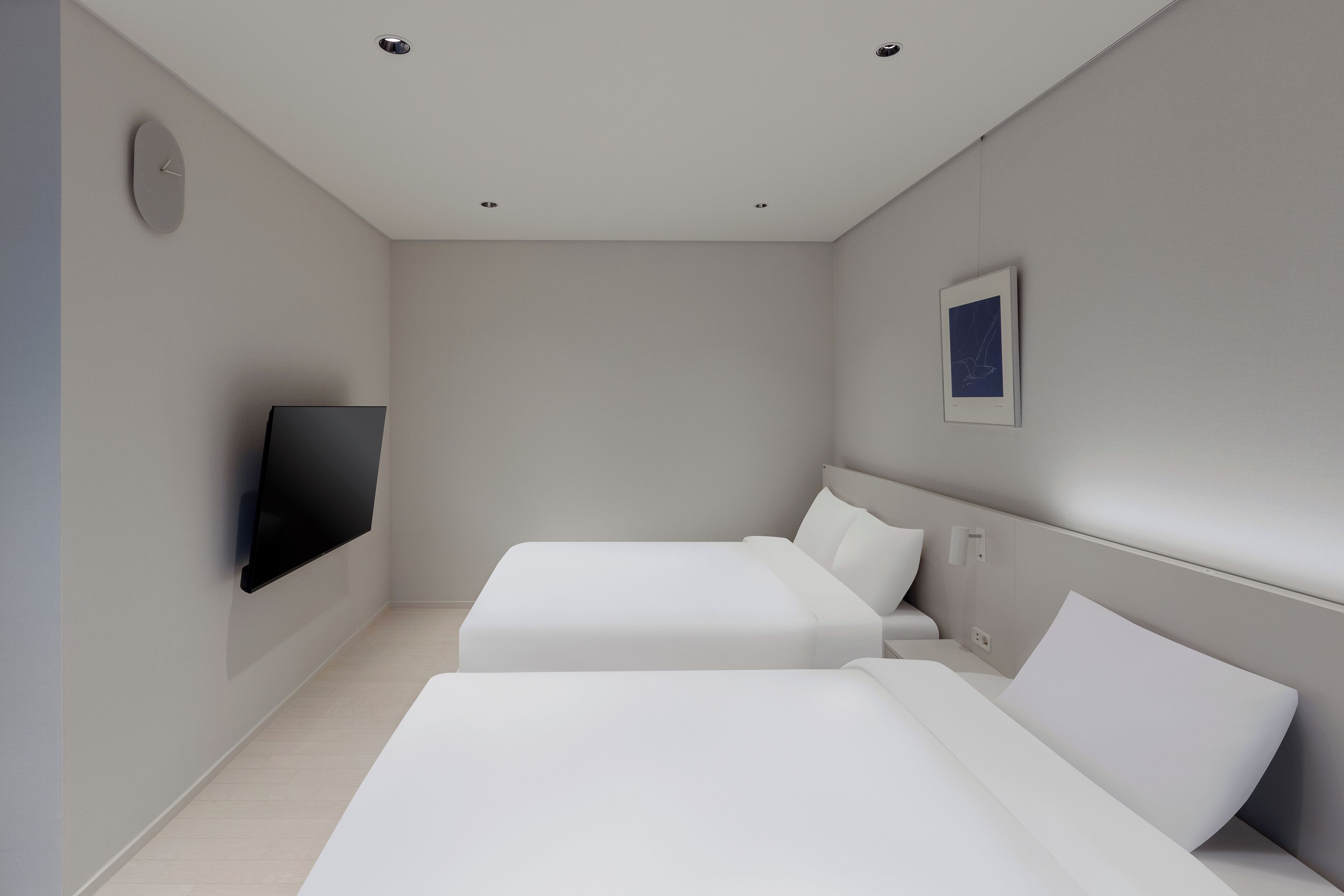 A modern hotel room with two beds, a flat-screen TV, and a framed picture on the wall.