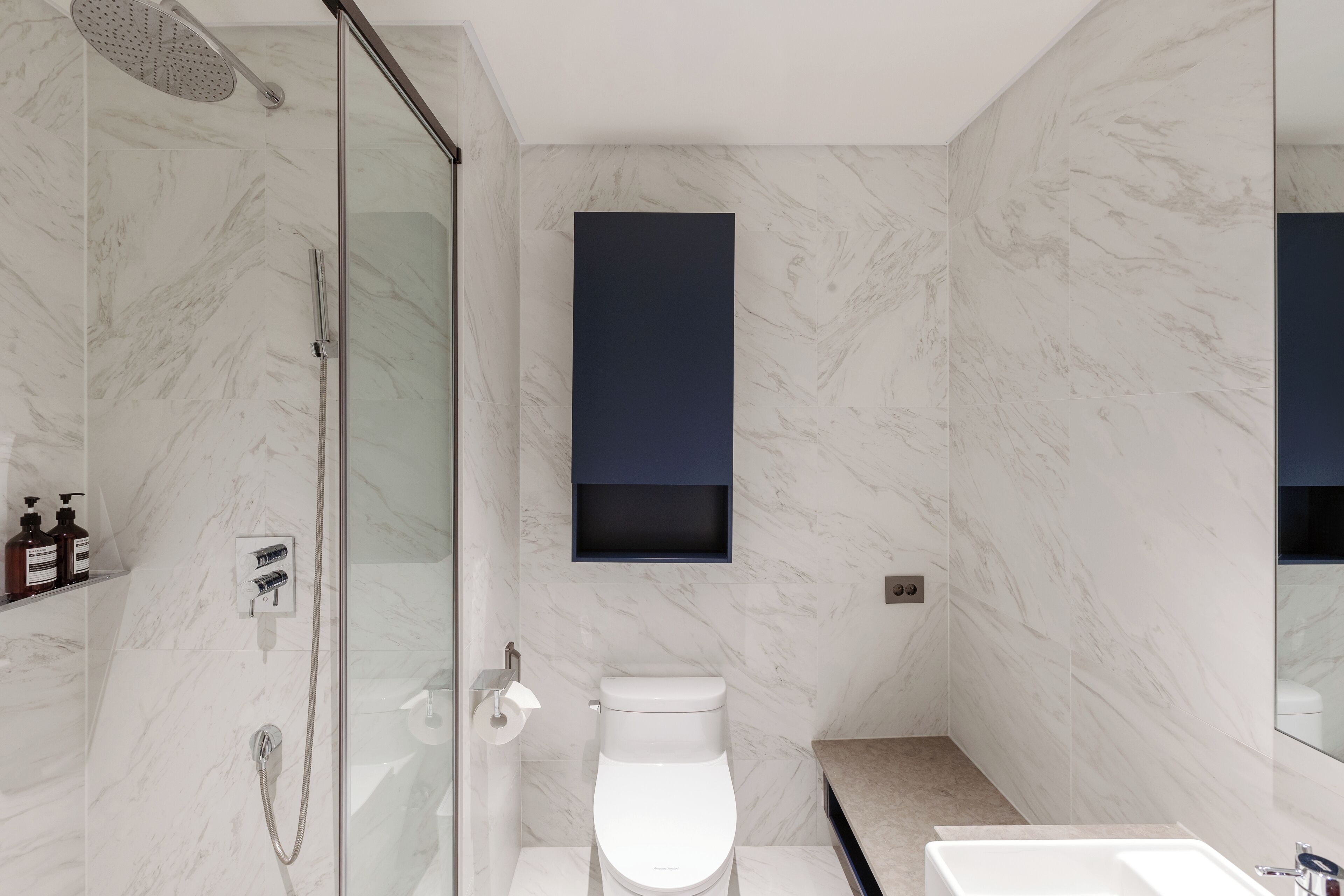 A modern bathroom with a glass-enclosed shower, a white toilet, and a large mirror.