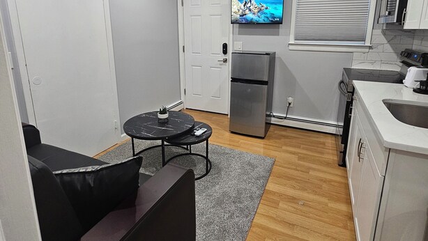 A compact living space with a sofa, a small round table, a kitchen area with a refrigerator, a microwave, and a sink.