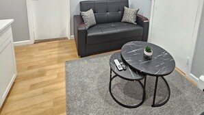 A modern living room with a grey sofa, a round coffee table with a plant, and a wooden floor.