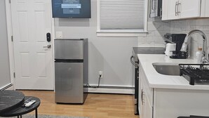 A compact kitchen with white cabinets, a built-in oven, a stainless steel refrigerator, a sink, and a small dining area with a table and chairs.