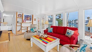 Un salon lumineux avec un canapé rouge, une table basse colorée et une vue sur le port de plaisance.
