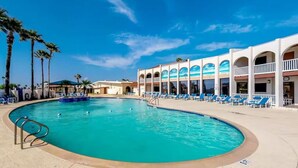 Un espace piscine doté d’une piscine aux formes arrondies, de chaises longues et d’un bâtiment agrémenté de fenêtres en arc de cercle et de balcons.