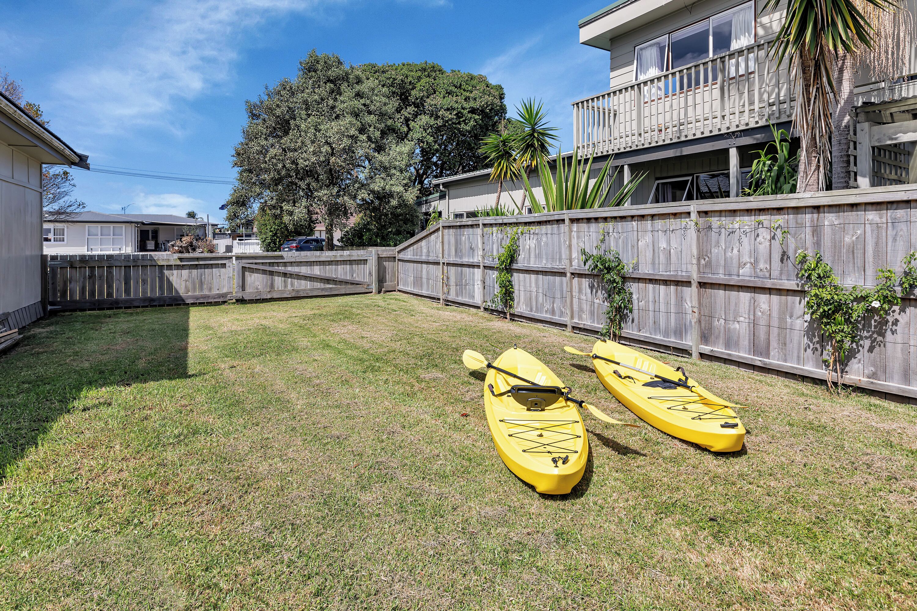 A backyard with two yellow kayaks, a wooden fence, and a building with a balcony.