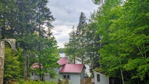 Punakatolla varustettu mökki, jonka ympärillä on tiheä metsä ja jonka edessä on sorapäällysteinen ajotie.