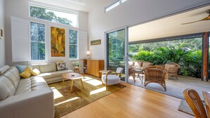 Een moderne woonkamer met een bank, salontafel en stoelen, grote ramen en uitzicht op groen.