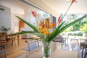 A dining area with a clear view of the outdoors, a glass vase with flowers, and a wooden table. - Brunswick Lux - Close to Creek & Beach (Brunswick Heads)