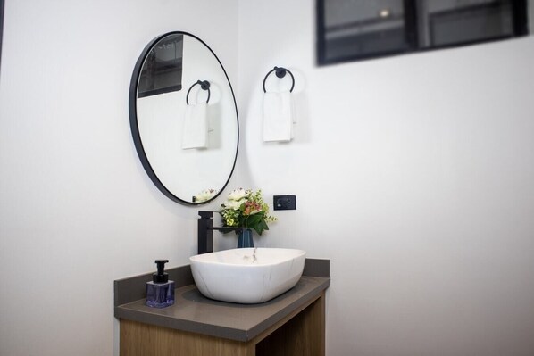 A modern bathroom with a white sink, a round mirror, and a vase with flowers.