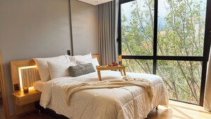 A modern bedroom with a large window, a bedside table with a lamp, and a tray with fruits and a glass of orange juice. - Rosa Negra Stadio | Your Cozy Getaway (Medellín)