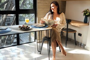 A person reading a book at a table with a glass of orange juice and a plate of fruit. - Cozy Aparta-Suite Studio | Rosa Negra (Medellín)