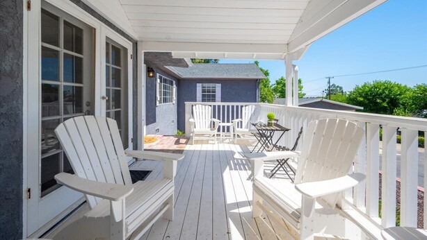 A covered porch with white Adirondack chairs and a table, a small blue house in the background, and a clear blue sky. - Bohemian Oasis on Vine (Paso Robles)