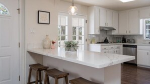 A kitchen with white cabinets, a marble countertop, and a pendant light. There are stools at the counter and a window with a view of trees. - Bohemian Oasis on Vine (Paso Robles)