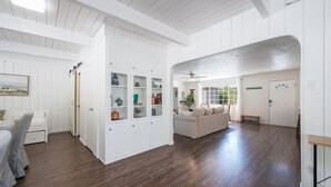 A spacious room with a high ceiling, wooden flooring, a built-in white cabinet with glass doors, a white sofa, and a ceiling fan. - Bohemian Oasis on Vine (Paso Robles)