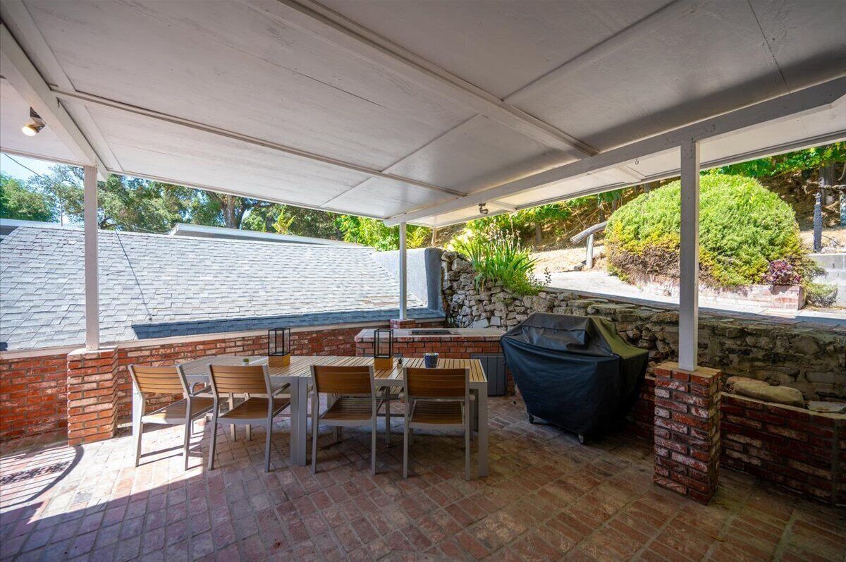 Une terrasse extérieure dotée d’un espace salon couvert, d’un barbecue et d’un mur en pierre.