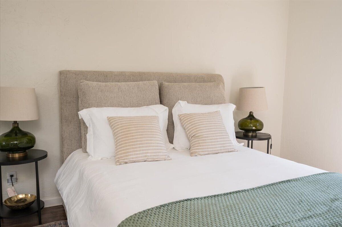 A neatly made bed with a white comforter and two striped pillows, flanked by two small side tables with lamps.