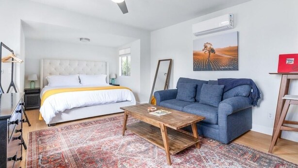A modern hotel room with a bed, a sofa, a coffee table, a ceiling fan, and a large window.