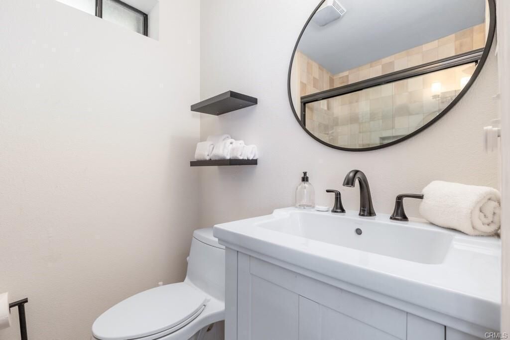 A modern bathroom with a white sink, black faucets, a round mirror, and a toilet.