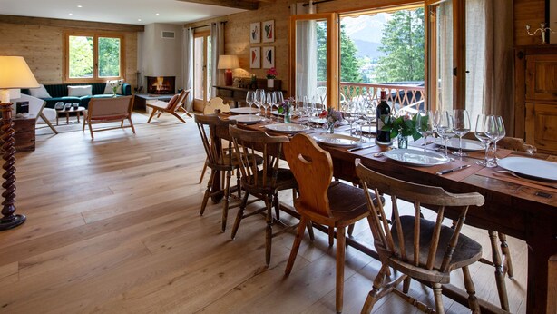 Ein Holzinnenraum mit Essbereich, gedecktem Tisch, Kamin und großen Fenstern mit Blick ins Freie.