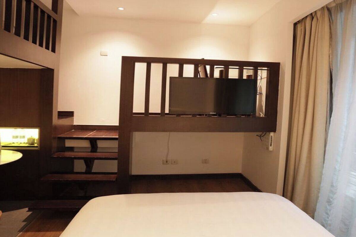 A hotel room with a bunk bed, a television mounted on a wooden partition, a desk with a chair, and a window with curtains.