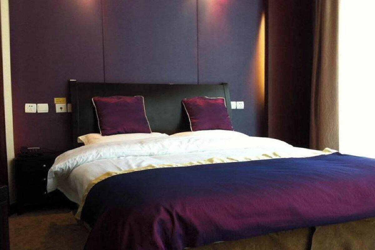 A neatly made bed with a dark headboard and two pillows, a bedside table with a lamp, and a window with curtains.