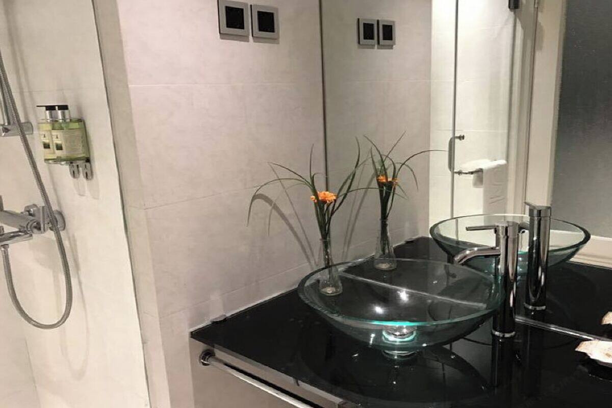 A modern bathroom with a glass sink, a handheld showerhead, and a mirror.