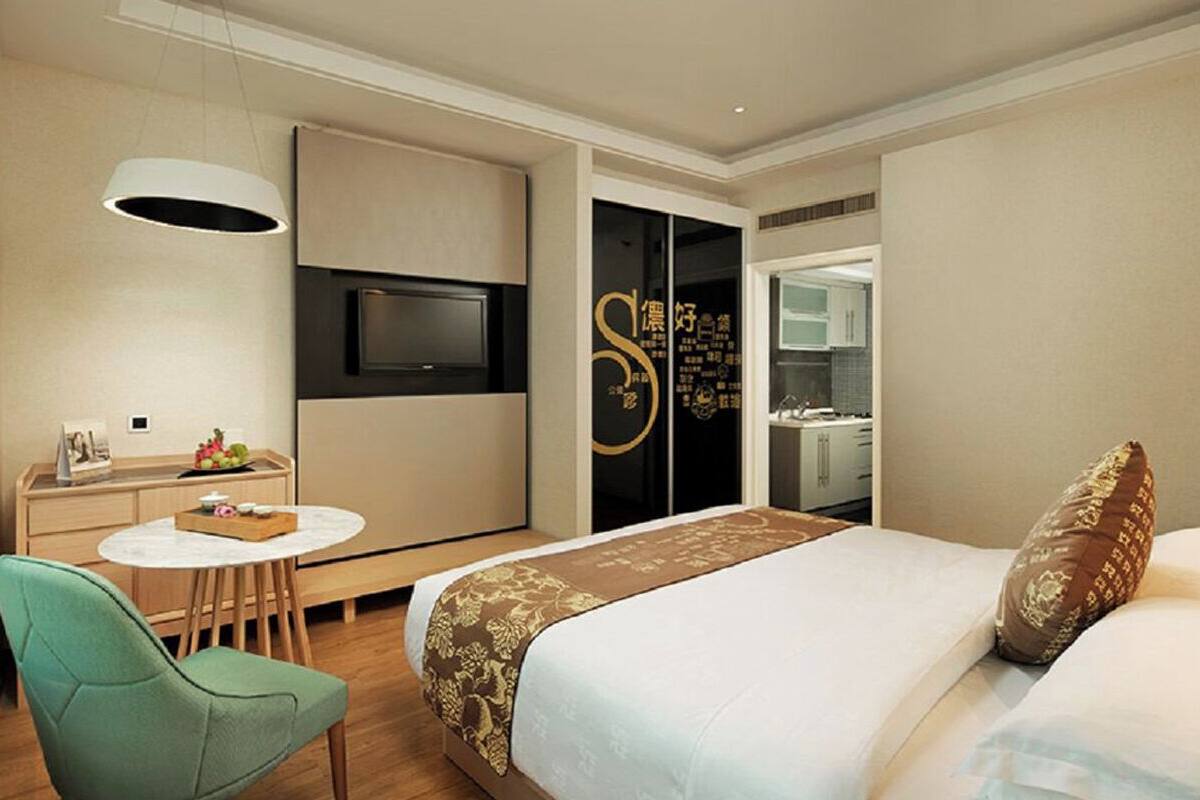 A hotel room with a bed, a desk, a chair, a TV, and a wardrobe.