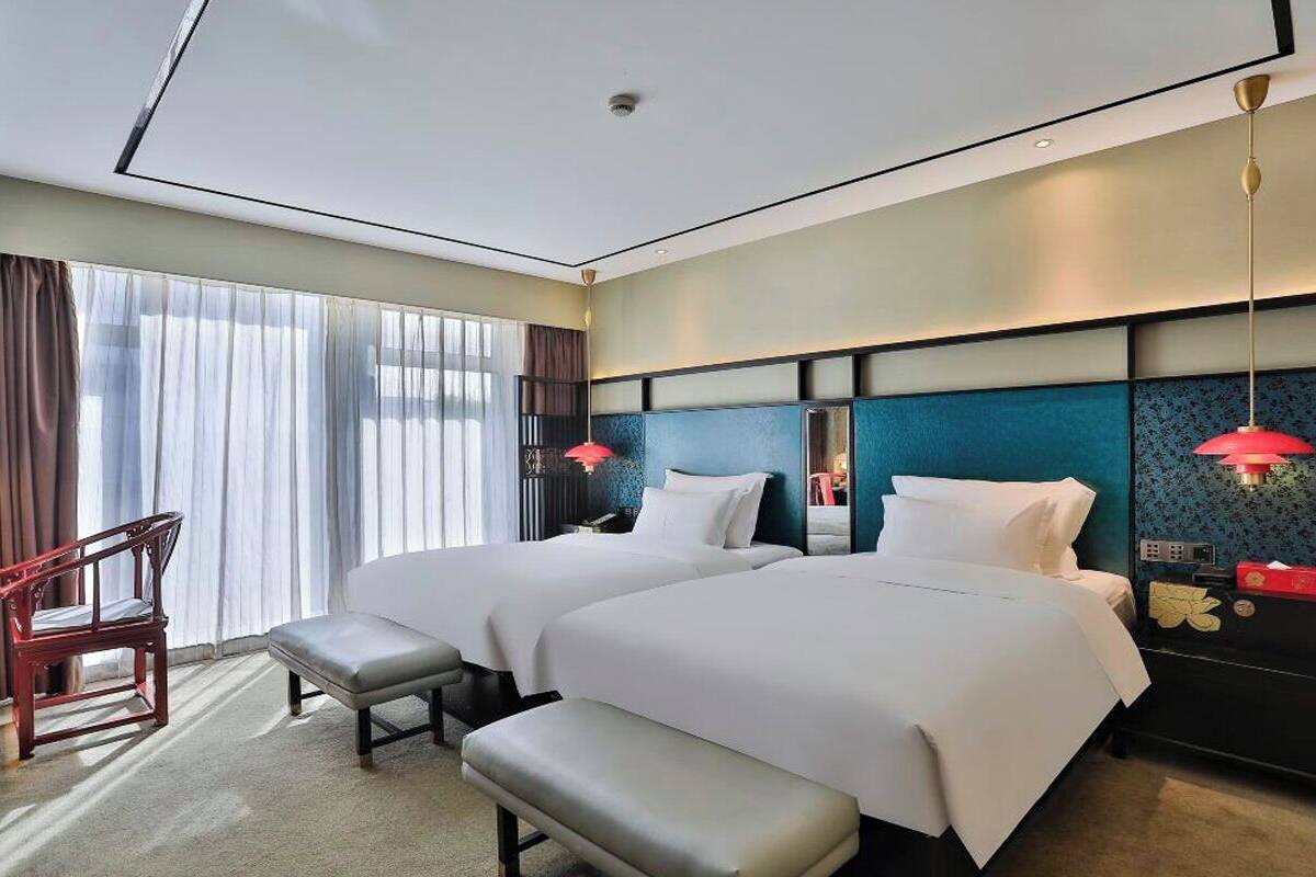 A hotel room with two beds, a bench, a desk, and a chair.