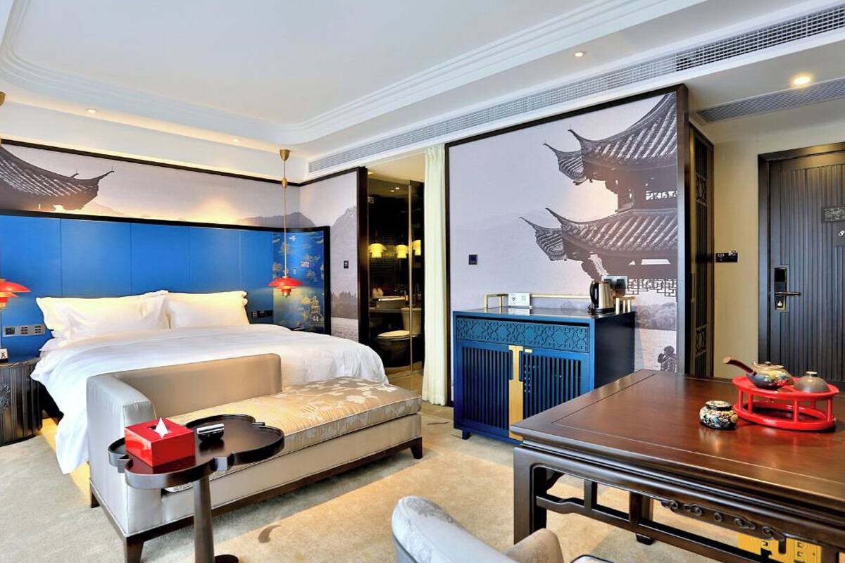 A modern hotel room with a large bed, a dining table, and a traditional Asian-style mural.