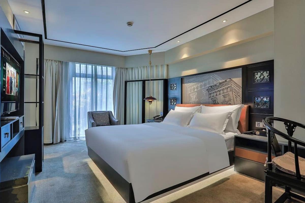 A modern hotel room with a large bed, a desk, a chair, and a TV.