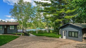 A cabin with a gravel driveway, a wooden deck, and a view of a lake. - Cabin w/Bunk on Whitefish Chain! (Crosslake)