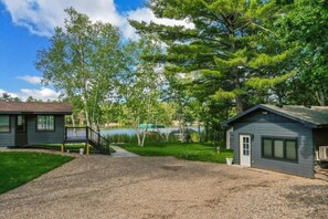 A cabin with a gravel driveway, a wooden deck, and a view of a lake.