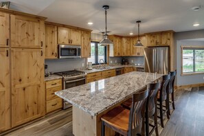A kitchen with wooden cabinets, granite countertops, stainless steel appliances, and a large island with bar stools. - Cabin w/Bunk on Whitefish Chain! (Crosslake)