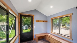 A room with a black door, wooden bench, and a window with a view of a yard. - Cabin w/Bunk on Whitefish Chain! (Crosslake)