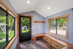 Una habitación con una puerta negra, un banco de madera y una ventana que da a un patio.