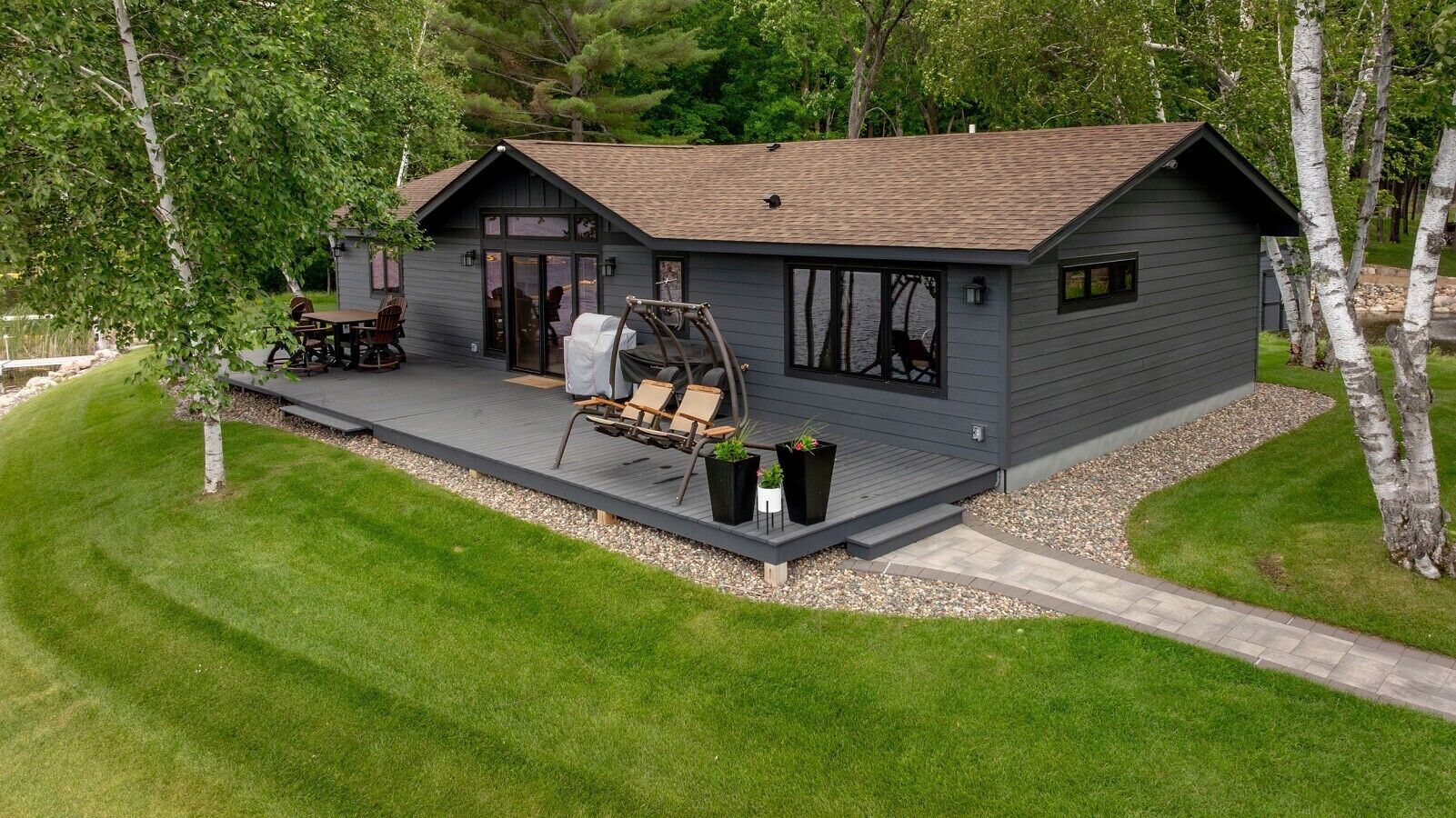 A modern cabin with a deck, outdoor seating, and a large window overlooking a natural landscape.