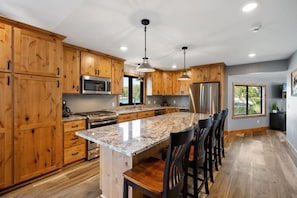 A modern kitchen with wooden cabinets, stainless steel appliances, a granite countertop, and a bar area with chairs. - Cabin w/Bunk on Whitefish Chain! (Crosslake)