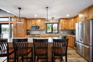 Cocina moderna con armarios de madera, encimeras de granito, electrodomésticos de acero inoxidable y una zona de bar con sillas.