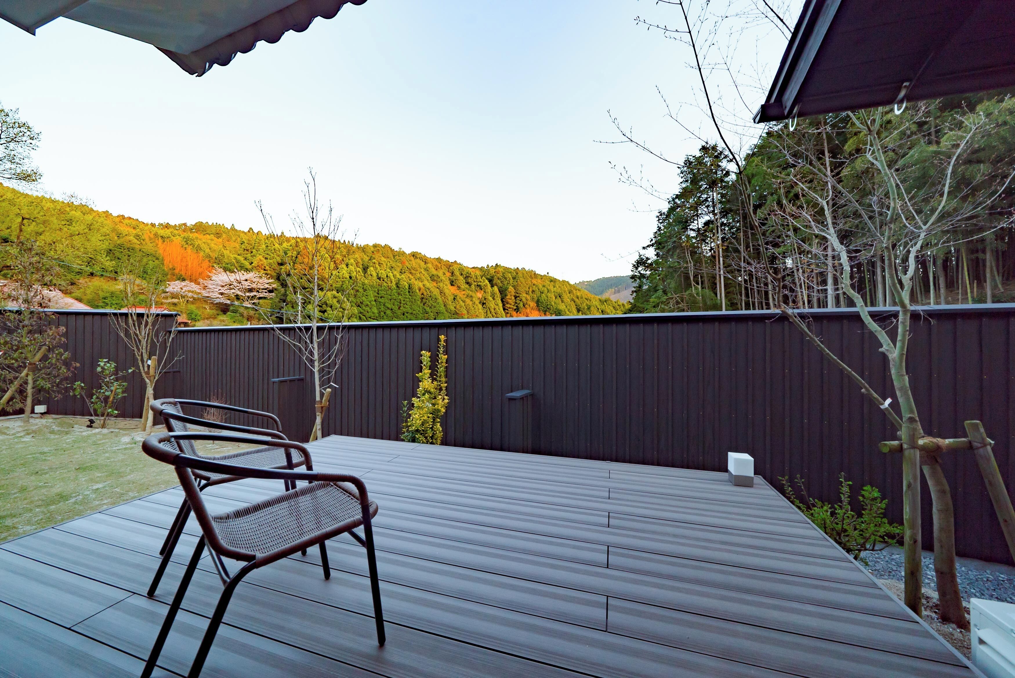A deck with two metal chairs, a dark wooden floor, and a view of a forested hillside.