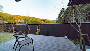 A deck with two metal chairs, a dark wooden floor, and a view of a forested hillside.