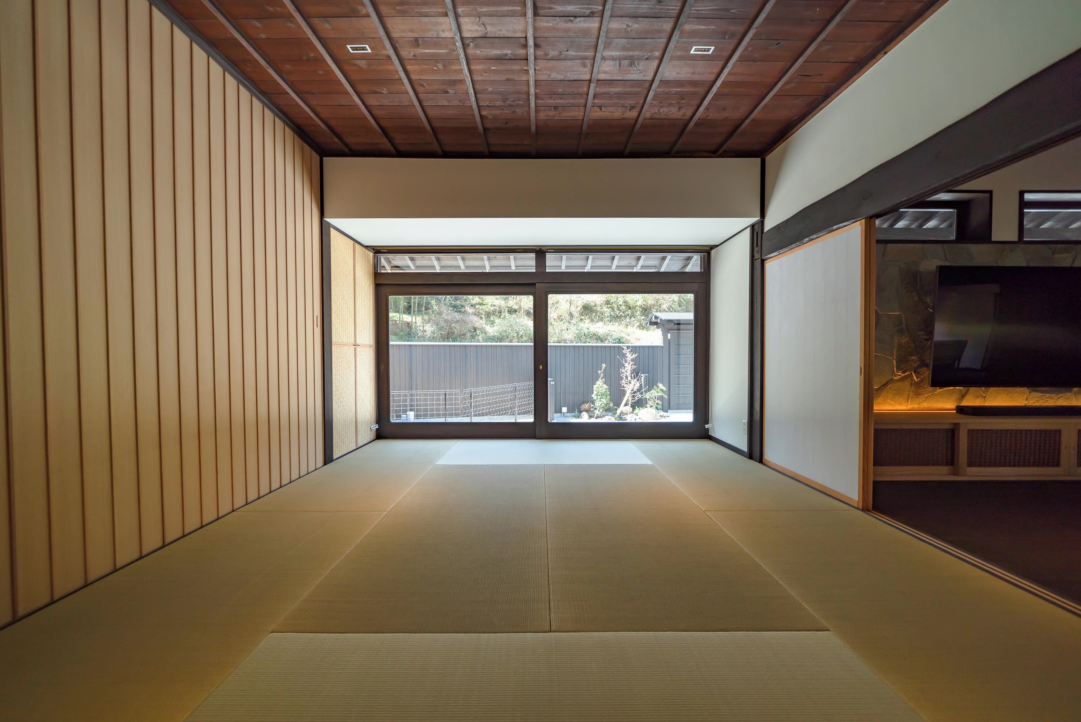 A tatami mat room with sliding doors, a wooden ceiling, and a view of the outside.
