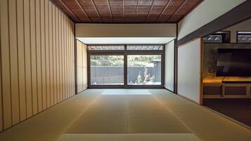 A tatami mat room with sliding doors, a wooden ceiling, and a view of the outside.