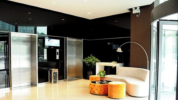 A modern lobby with a glass wall, a white sofa, and a round coffee table. - StarChain Qijiang Hotel - Zhongshan Xingzhong Square Sunwen Pedestrian Street Branch  (Zhongshan)