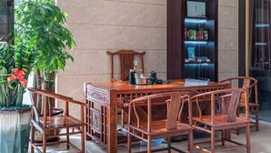 A wooden dining table with chairs, a potted plant, and a cabinet with illuminated shelves. - StarChain Qijiang Hotel - Zhongshan Xingzhong Square Sunwen Pedestrian Street Branch  (Zhongshan)