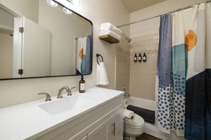 Een badkamer met een witte wastafel, twee kraanwerkstukken, een spiegel, een handdoekhouder, een toilet en een douchegordijn.