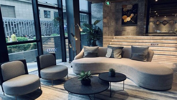 A modern lounge area with a curved sofa, two armchairs, and a coffee table, featuring a large window with a view of the street. - StarChain Shenzhen Bay Hotel (Shenzhen Bay Port Branch) (Shenzhen)