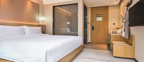 A modern hotel room with a large bed, a wooden headboard, a small bedside table, a mirror, and a television.