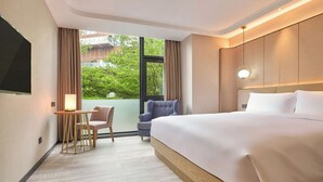 A modern hotel room with a large bed, a small table with a chair, a TV, and a view of greenery outside. - StarChain Shenzhen Bay Hotel (Shenzhen Bay Port Branch) (Shenzhen)