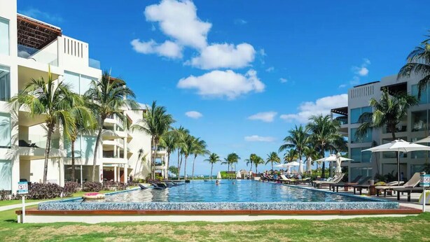 A resort pool area with palm trees, lounge chairs, and a clear blue sky.