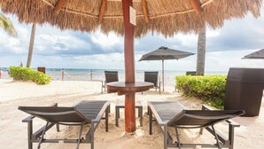 A beachside lounge with thatched umbrellas, lounge chairs, and a view of the ocean.