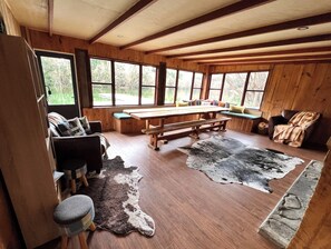 A rustic cabin interior with wooden walls, large windows, a wooden dining table, benches, and a fur rug. - Private lake with lodgings for 15 people. Ultimate family getaway! (Fairlie)